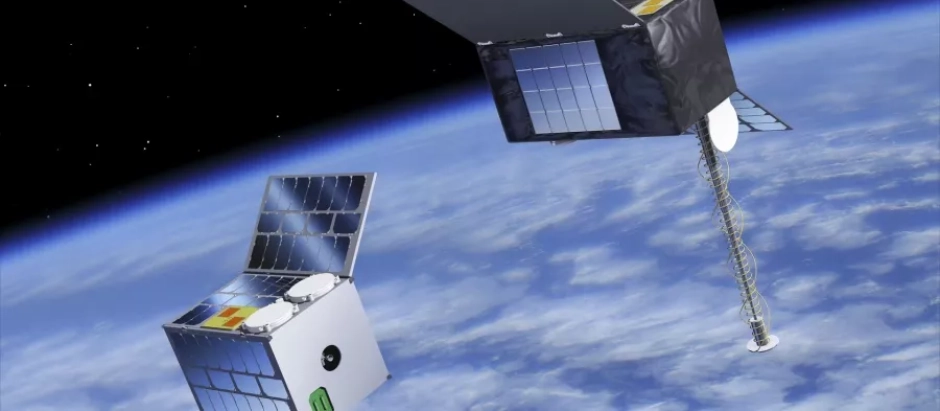 Imagen de dos satélites tipo Cubesat desplegados en órbita terrestre baja. Están conectados por un largo cable o estructura, posiblemente para pruebas de tecnología espacial o experimentos de formación en vuelo. La Tierra se ve en el fondo con nubes visibles y el espacio oscuro arriba.