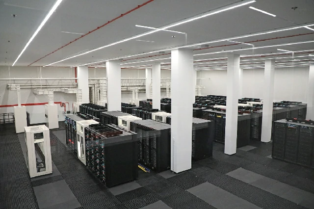 Vista interior de un amplio centro de datos con filas de servidores de alta capacidad en un entorno con iluminación blanca y columnas de soporte, probablemente representando las instalaciones del superordenador MareNostrum.