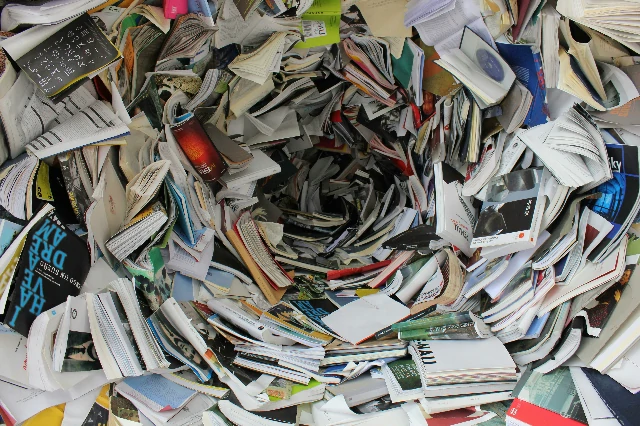 Una pila desordenada de libros y revistas con páginas dobladas y tapas abiertas, acumulados en un montón caótico, sugiriendo un contexto de reciclaje o desecho.